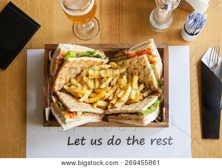 Four Small Sandwiches And French Fries In A Wooden Plate On A Table.