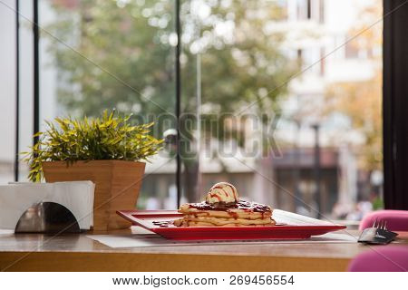 Chocolate Waffle Topped With Ice Cream And Strawberry Decoration On Red Plate.