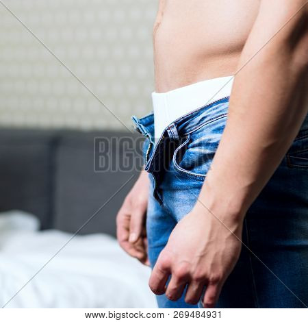 Young Man With Athletic Body Unzips His Jeans In The Bedrom.