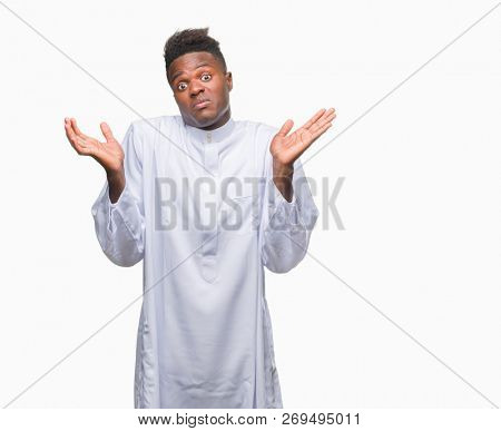 Young arabic african man wearing traditional djellaba over isolated background clueless and confused expression with arms and hands raised. Doubt concept.