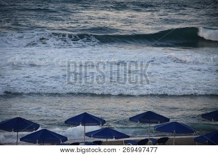Big Wave On A Beach With Umbrellas