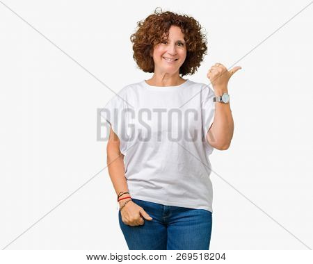 Beautiful middle ager senior woman wearing white t-shirt over isolated background smiling with happy face looking and pointing to the side with thumb up.