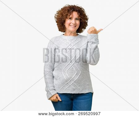 Beautiful middle ager senior woman wearing winter sweater over isolated background smiling with happy face looking and pointing to the side with thumb up.