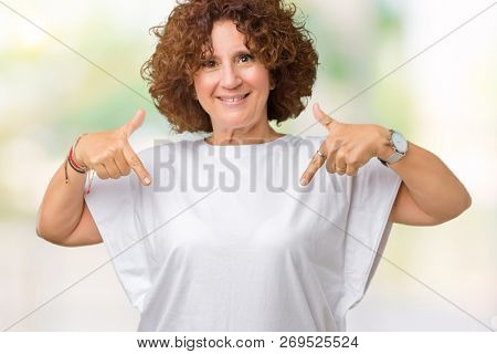 Beautiful middle ager senior woman wearing white t-shirt over isolated background looking confident with smile on face, pointing oneself with fingers proud and happy.