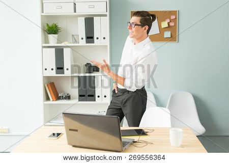 Business, Office, People Concept - Handsome Man In Glasses Stands In The Office Near A Computer And 