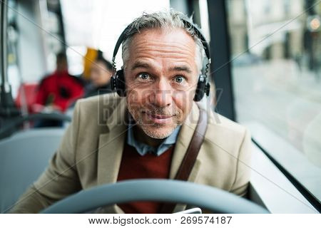 Mature Tired Businessman With Heaphones Travelling By Bus In City.