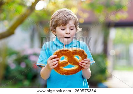 Adorable Little Kid Boy Eating Huge Big Bavarian German Pretzel. Happy Blond Child Enjoying Tasteful