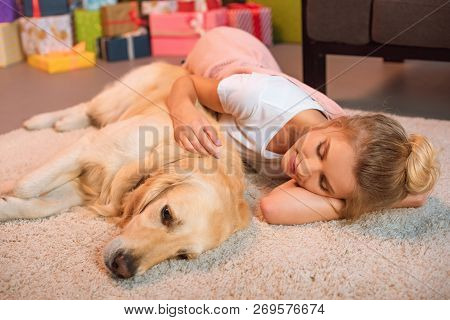 Beautiful Young Blonde Woman Lying On Floor And Hugging Golden Retriever Dog At Home On Fluffy Rug A