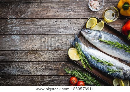 Fresh Raw Seabass And Ingredients For Cooking. Two Fish Seabass With Lemon, Spices And Herbs On Wood