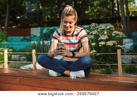 Portrait of a happy young teenage girl sitting on a bench at the park, looking a tmobile phone, laughing
