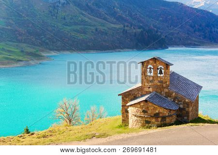 Sunny picturesque view of stone chapel on Roselend lake (Lac de Roselend) in France Alps (Auvergne-Rhone-Alpes). Landscape photography