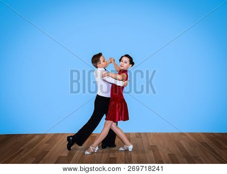 The Young Boy And Girl Posing At Dance Studio On Gray. The Ballroom Dancing Concept