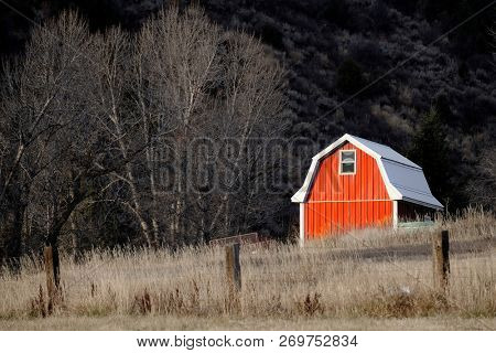 Old red barn in field late fall or autumn brown grass and fence