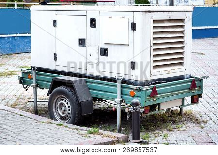 Backup Power Generator Mounted On A Car Trailer On Wheels Standing On A City Street Paved With Pavin