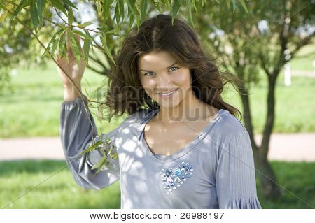 Beautiful smiling girl against a backdrop of green branches