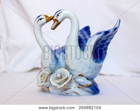 Two Porcelain Swans On A Light Background. Statue Of Two Swans In Love.