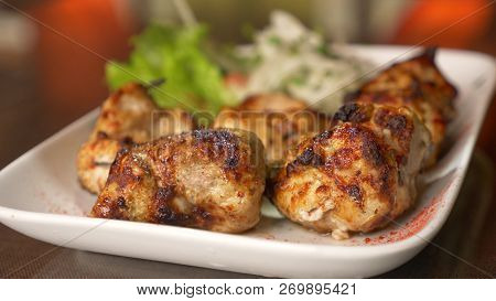 Close Of Roasted Meat Lying On A White Plate With Greens On A Table
