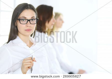 Attractive Businesswoman At Meeting Or Conference Against The Background Of Colleagues. Group Of Bus