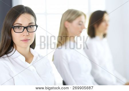 Attractive Businesswoman At Meeting Or Conference Against The Background Of Colleagues. Group Of Bus