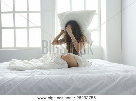 Young caucasian woman covering her head and ears with pillows.