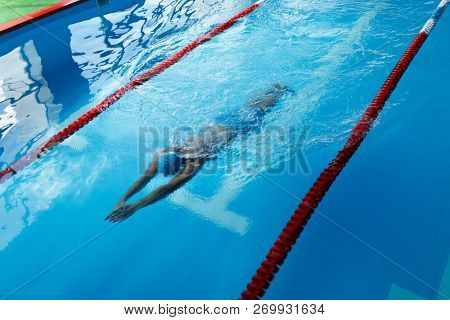 Photo of sportsman in blue cap swimming on path in pool