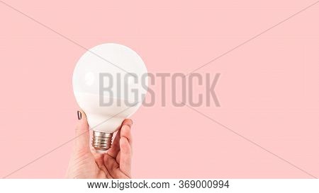 Female Hand Holding A Big White Matte Light Bulb On Terracotta Background, Close-up