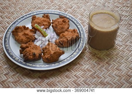 Side View Of Dal Vada, Masala Vada, Chana Vada Served With Cut Onion And Green Chilly And Tea On Ser