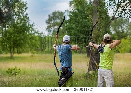 Two Men Aiming From Sports Bows At The Target. They Are Engaged In The Forest.