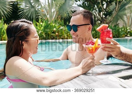 Happy Young Asian Couple Spending Honemoon In Swimming Pool And Enjoying Tasty Fruit Smoothie