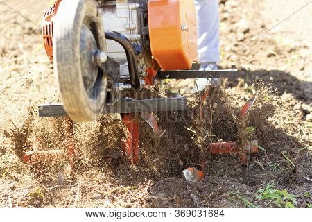 Man Farmer Plows The Land With A Cultivator. Agricultural Machinery: Cultivator For Tillage In The G