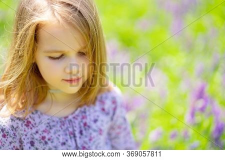 Small, Beautiful, Sad Girl Alone In A Field Of Purple Flowers. Child Is Unwell Because Of The Heat. 