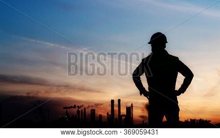 Rear View Of Silhouette Engineer Standing Outdoors By Oil Refinery At Dusk.