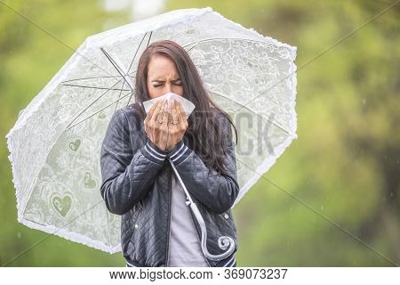 Girl Coughing Into A Napking Having A Flu, Walking Outside On A Rainy Day With An Umbrella.