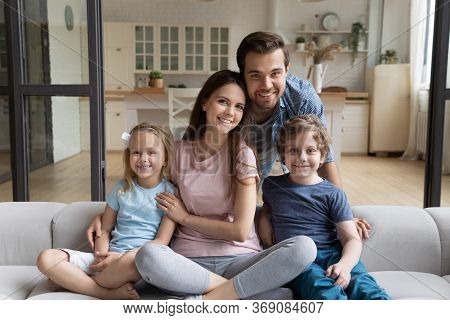 Portrait Of Smiling Young Parents Hug With Small Kids