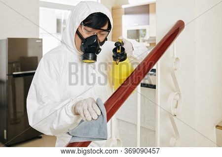 Specialist In Hazmat Suit Wiping Staircase Railing With Cleaning Spay To Kill Pathogens And Specific