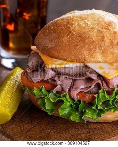 Roast Beef Sandwich With Cheese, Tomato And Lettuce On A Bun On A Wooden Cutting Board