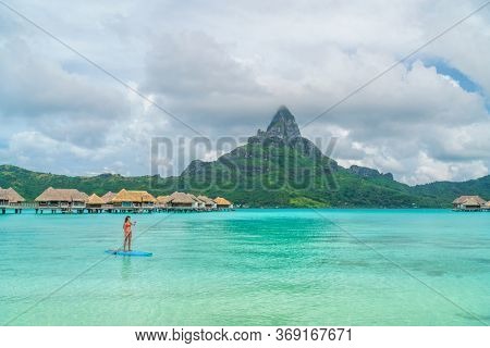 Tahiti beach vacation luxury resort hotel in Bora Bora, French Polynesia. Paddleboarding watersport leisure activity SUP paddle woman, French Polynesia. Mount Otemanu landscape summer holiday.