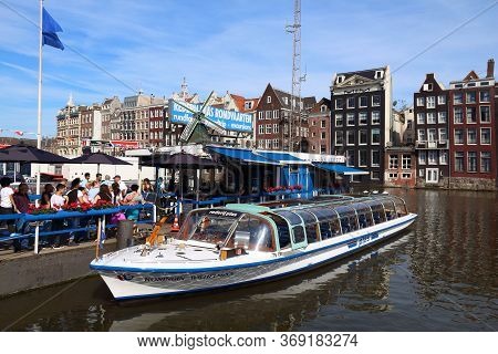 Amsterdam, Netherlands - July 9, 2017: People Wait For The City Tour Boat By Damrak Canal In Amsterd