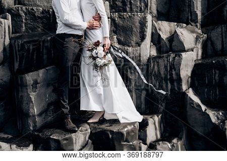 A Wedding Couple Stands On A Wall Of Stone Pillars. The Bride And Groom Are Hugging On Basalt Kekurs