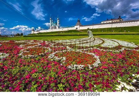 Colorful Flowerbed In The Form Of A Peacock Under A Blue Sky With White Clouds In Sunny Summer Weath
