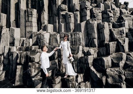 A Wedding Couple Stands On A Wall Of Stone Pillars. The Bride And Groom Are Hugging On Basalt Kekurs