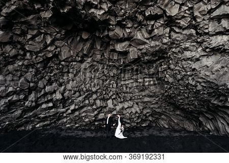 Destination Iceland Wedding. Wedding Couple Under A Rock Of Basalt Stones. Bride And Groom On The Bl