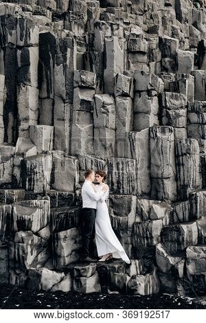 A Wedding Couple Stands On A Wall Of Stone Pillars. The Bride And Groom Are Hugging On Basalt Kekurs