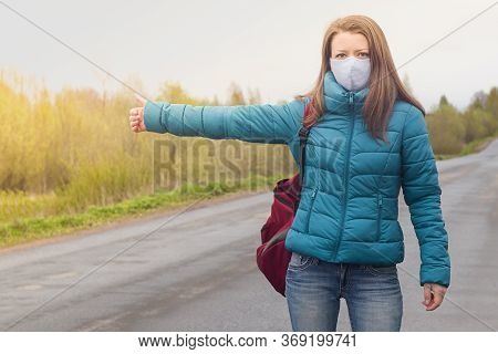 Girl In Protective Medical Facial Mask Catches A Car On The Road. Hitchhiking, Travaling Young Woman