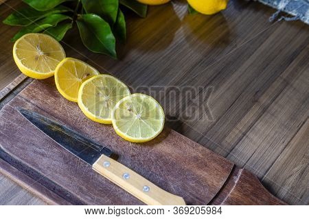 Some slices of lemon cut on a wooden board next to a knife on a rustic background