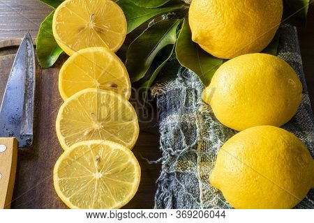 Some slices of lemon cut on a wooden board next to a knife on a rustic background