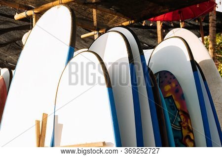 Close Up Set Of White Surfboard For Rent On The Beach In Sunshine. Multicolored Surf Boards Differen