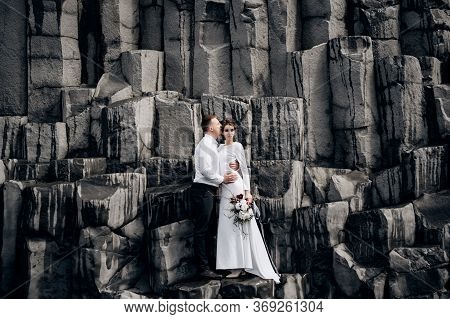 A Wedding Couple Stands On A Wall Of Stone Pillars. The Bride And Groom Are Hugging On Basalt Kekurs