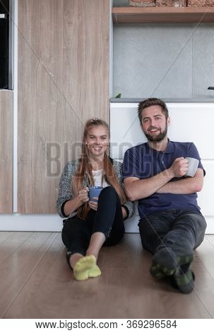 Happy young couple sitting at the kitchen flor smiling and holdi
