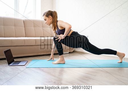Yoga. Beautiful Girl Athlete Engaged In Home, Makes Attacks. Online Sports On A Laptop. Stretching A